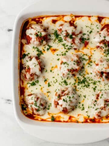 overhead view of finished meatball casserole in square white baking dish topped with chopped parsley