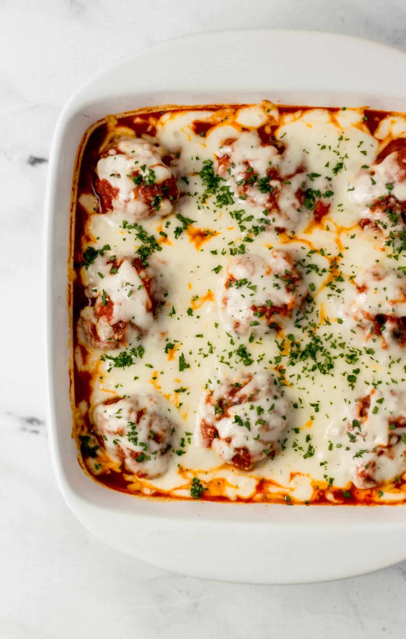 overhead view of finished meatball casserole in square white baking dish topped with chopped parsley 