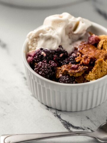 close up side view of single serving of cobbler in small white ramekin beside a spoon
