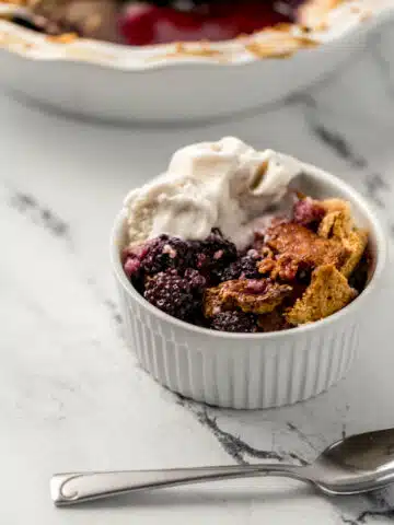 close up side view of single serving of cobbler in small white ramekin beside a spoon
