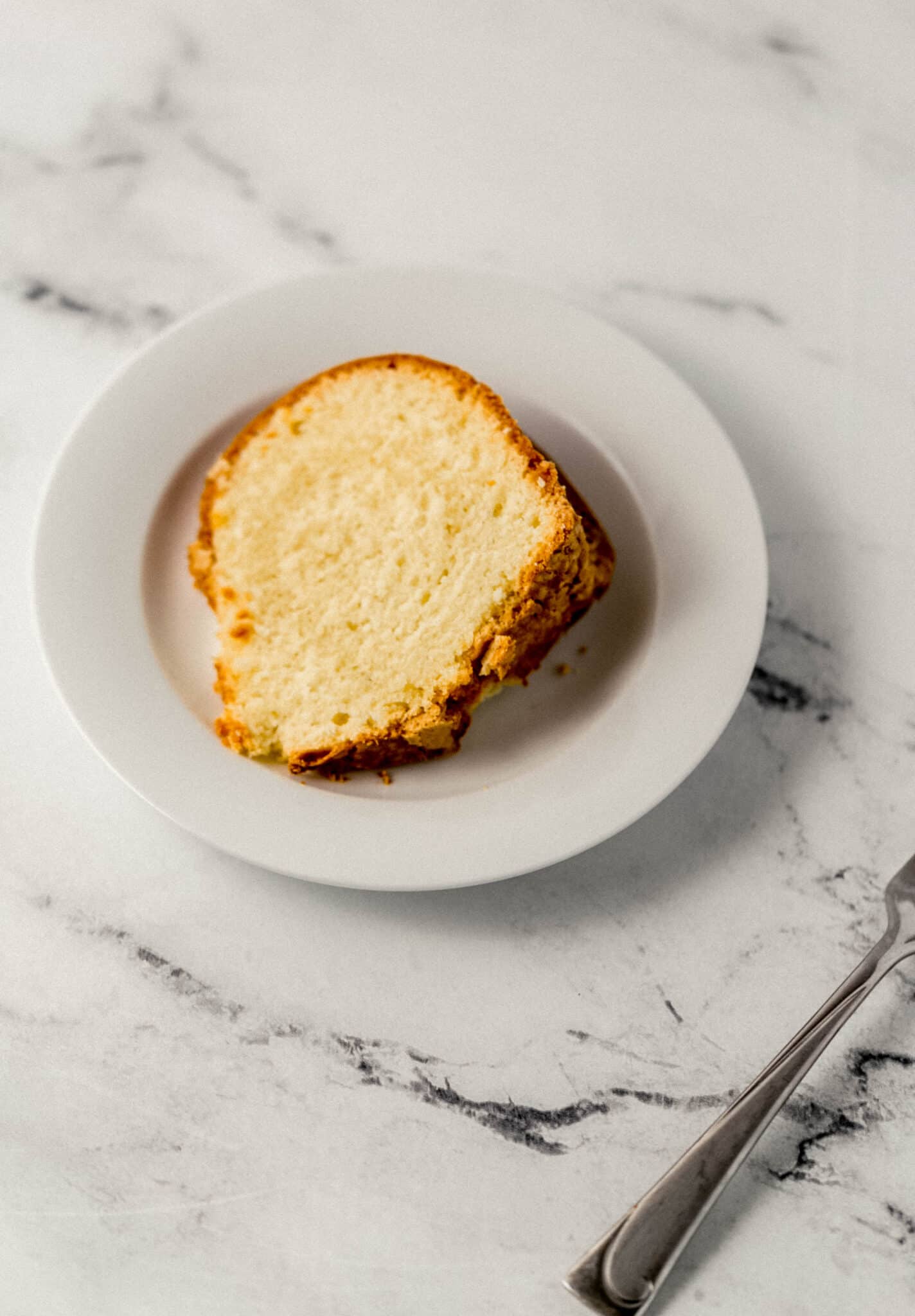 slice of pound cake on a white plate beside a fork 