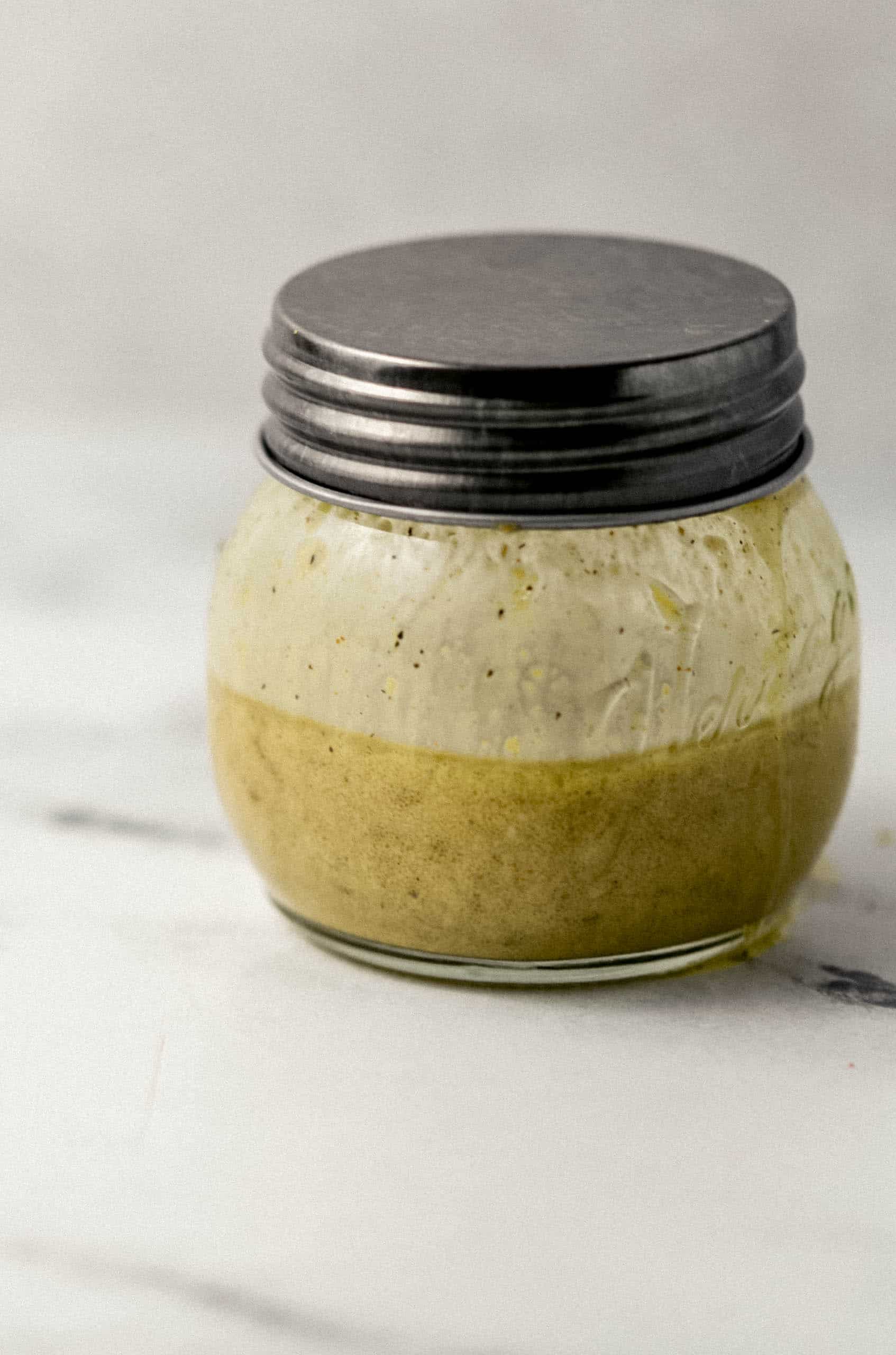 close up side view of salad dressing in small jar with lid on it. 