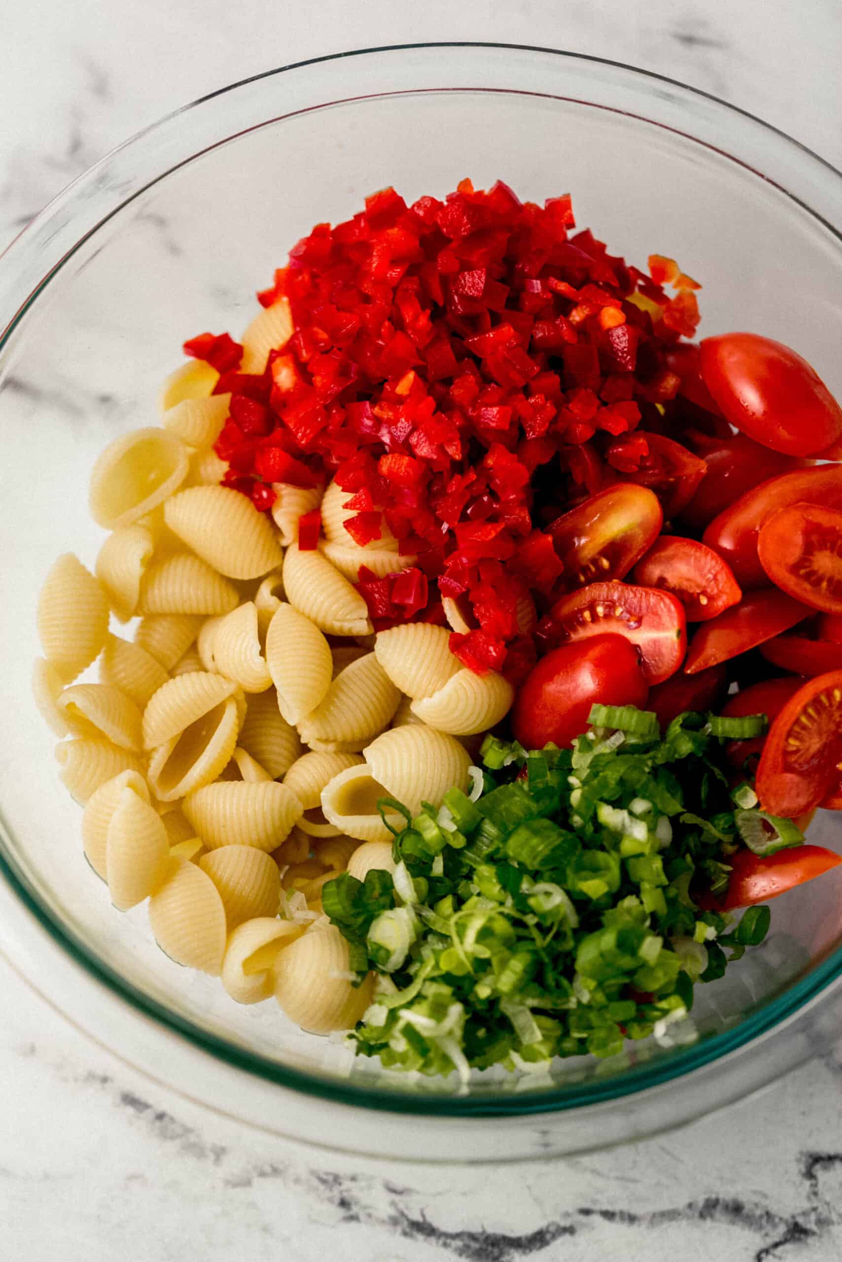 ingredients to make pasta salad added to large glass mixing bowl 