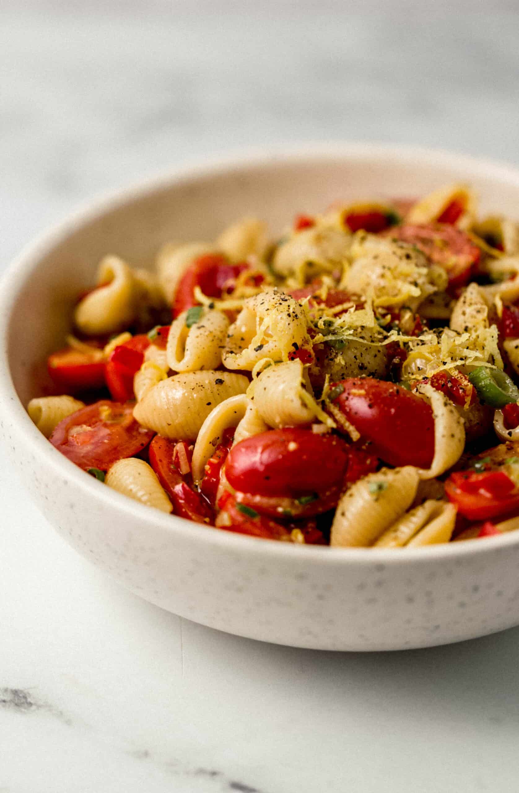 close up sideview of finished pasta salad in bowl topped with lemon zest and black pepper 