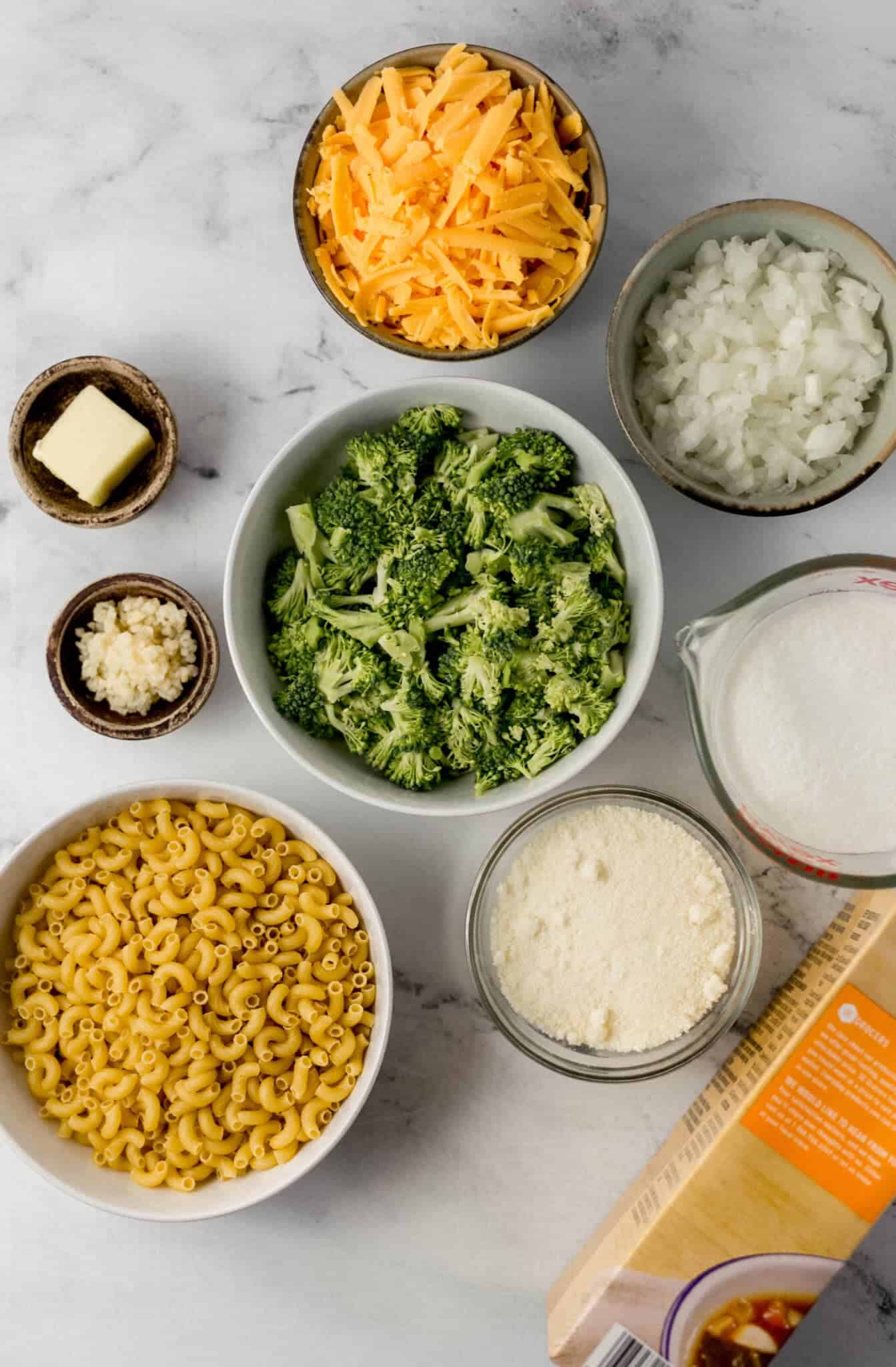 overhead view of ingredients needed to make pasta in separate bowls and containers on marble surface