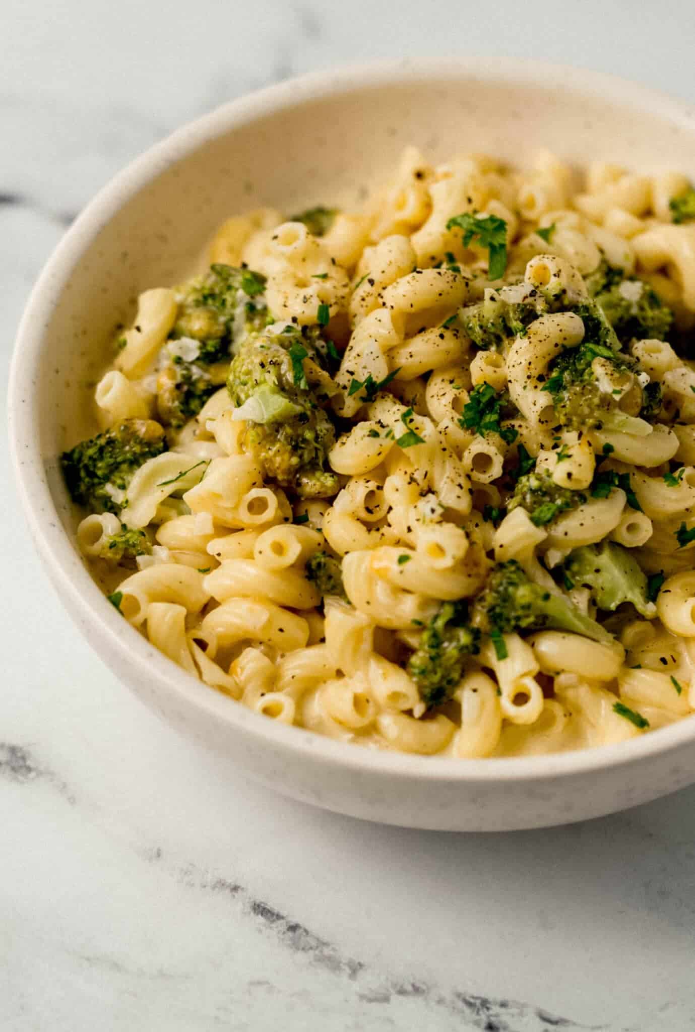 close up side view of finished pasta in white bowl topped with ground black pepper and chopped fresh parsley