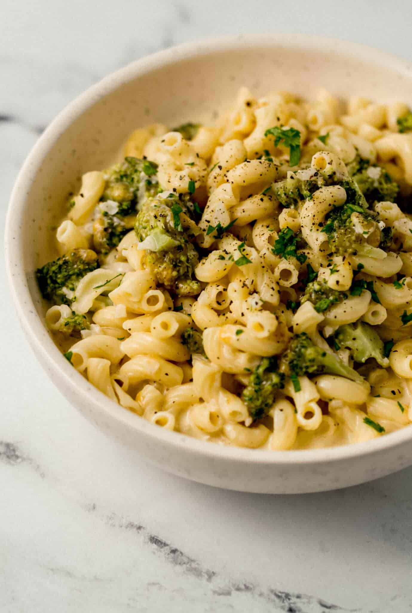 close up side view of finished pasta in white bowl topped with ground black pepper and chopped fresh parsley 