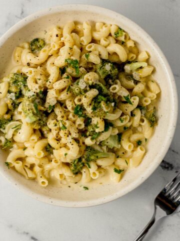 overhead view of bowl of finished pasta beside a fork on marble surface