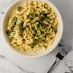 overhead view of bowl of finished pasta beside a fork on marble surface