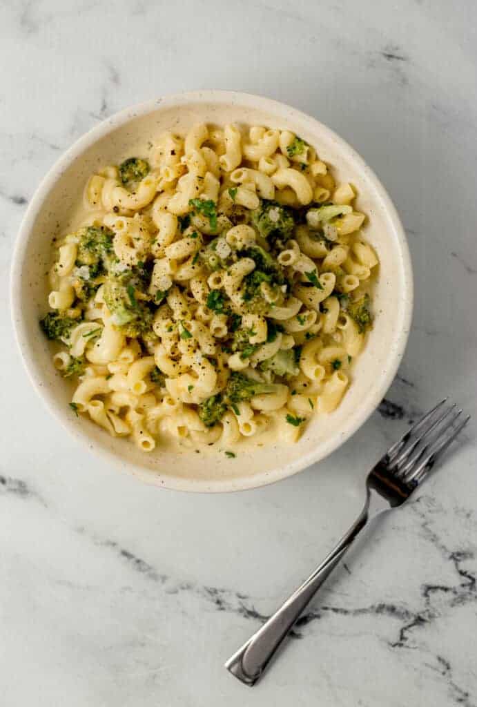 overhead view of bowl of finished pasta beside a fork on marble surface