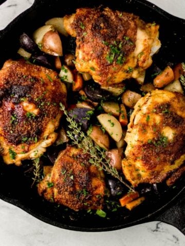 overhead view of finished chicken and vegetables in cast iron skillet on marble surface