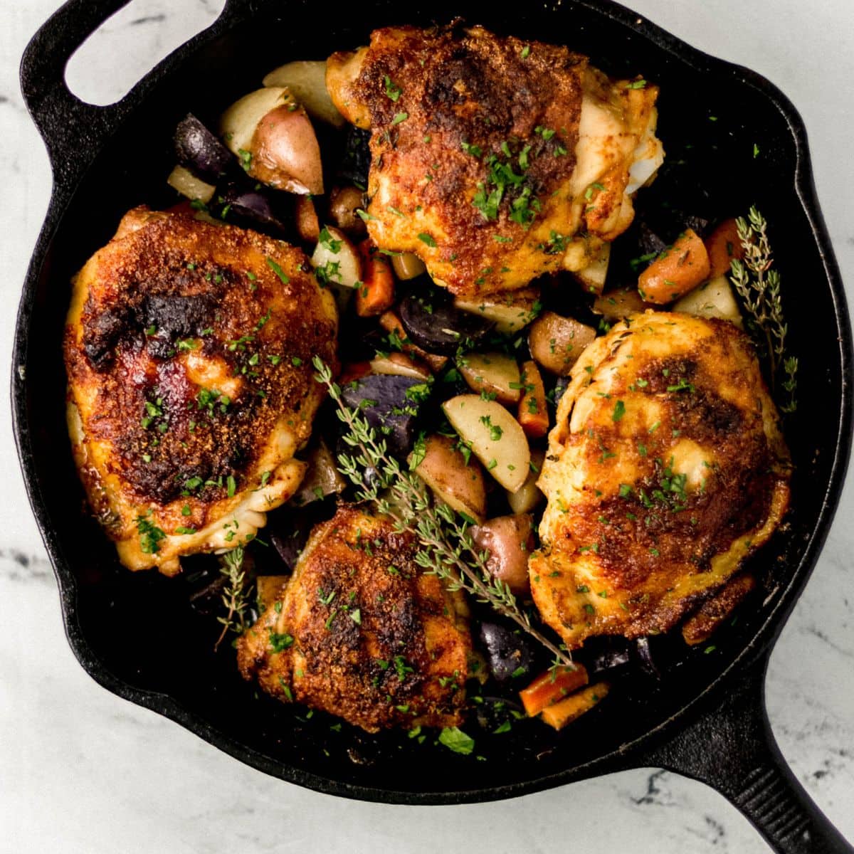 overhead view of finished chicken and vegetables in cast iron skillet on marble surface