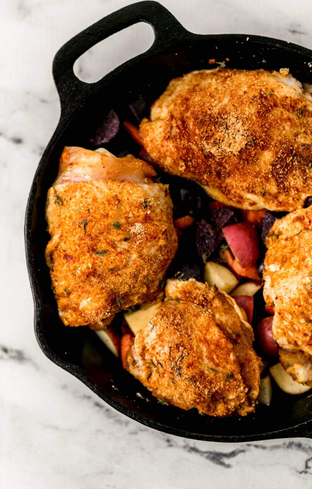 seasoned chicken added to cast iron skillet on top of seasoned carrots and potatoes, before baking