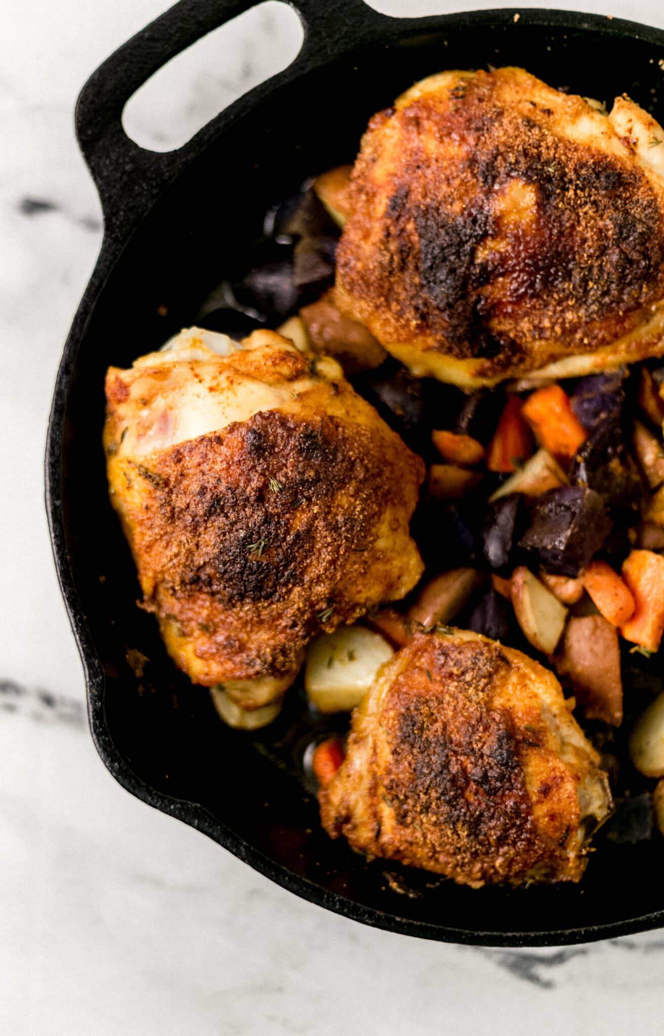 finished chicken thighs and veggies in cast iron skillet 