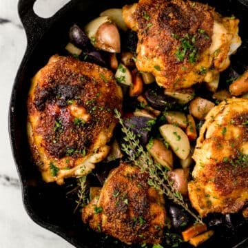 overhead view of baked chicken and vegetables in cast iron skillet topped with fresh thyme
