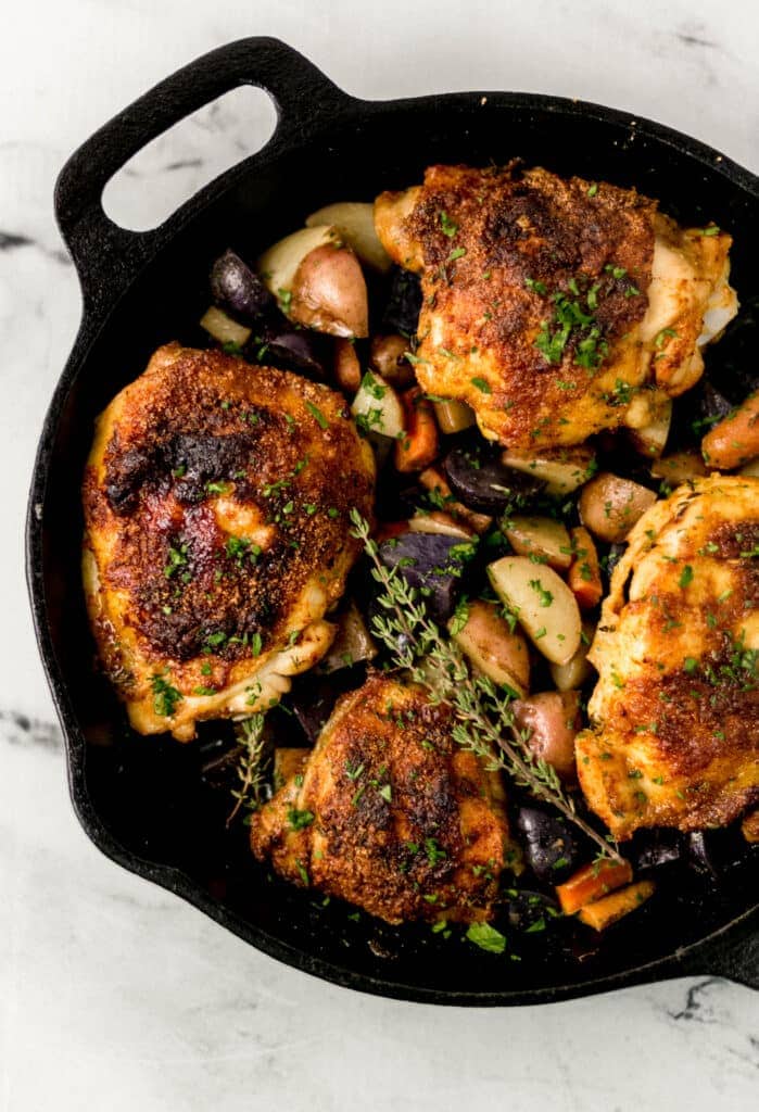 overhead view of baked chicken and vegetables in cast iron skillet topped with fresh thyme