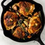 overhead view of finished chicken and vegetables in cast iron skillet on marble surface