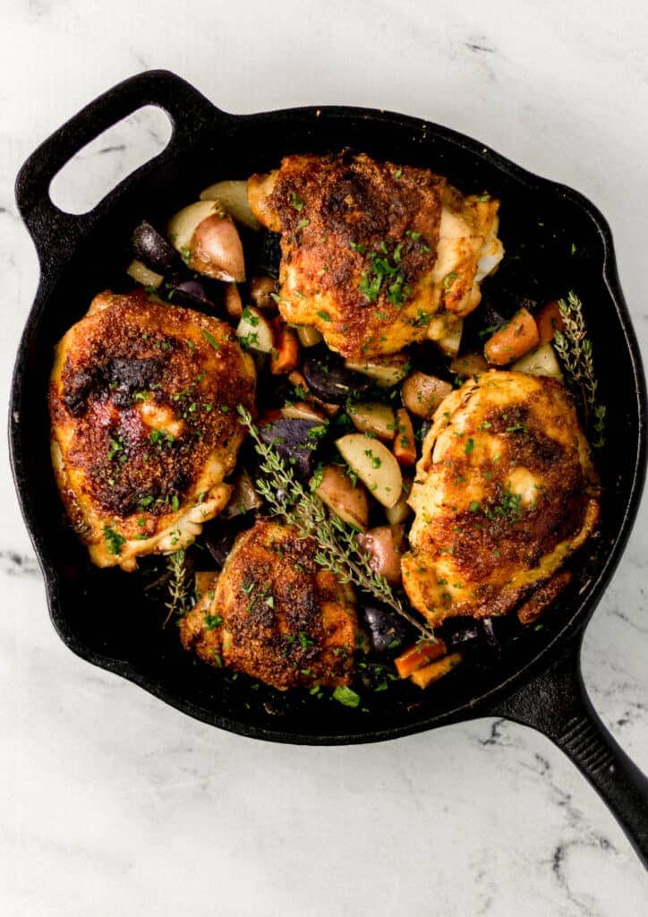 overhead view of finished chicken and vegetables in cast iron skillet on marble surface