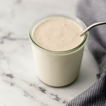 close up side view of milkshake in glass with straw in it beside cloth napkin