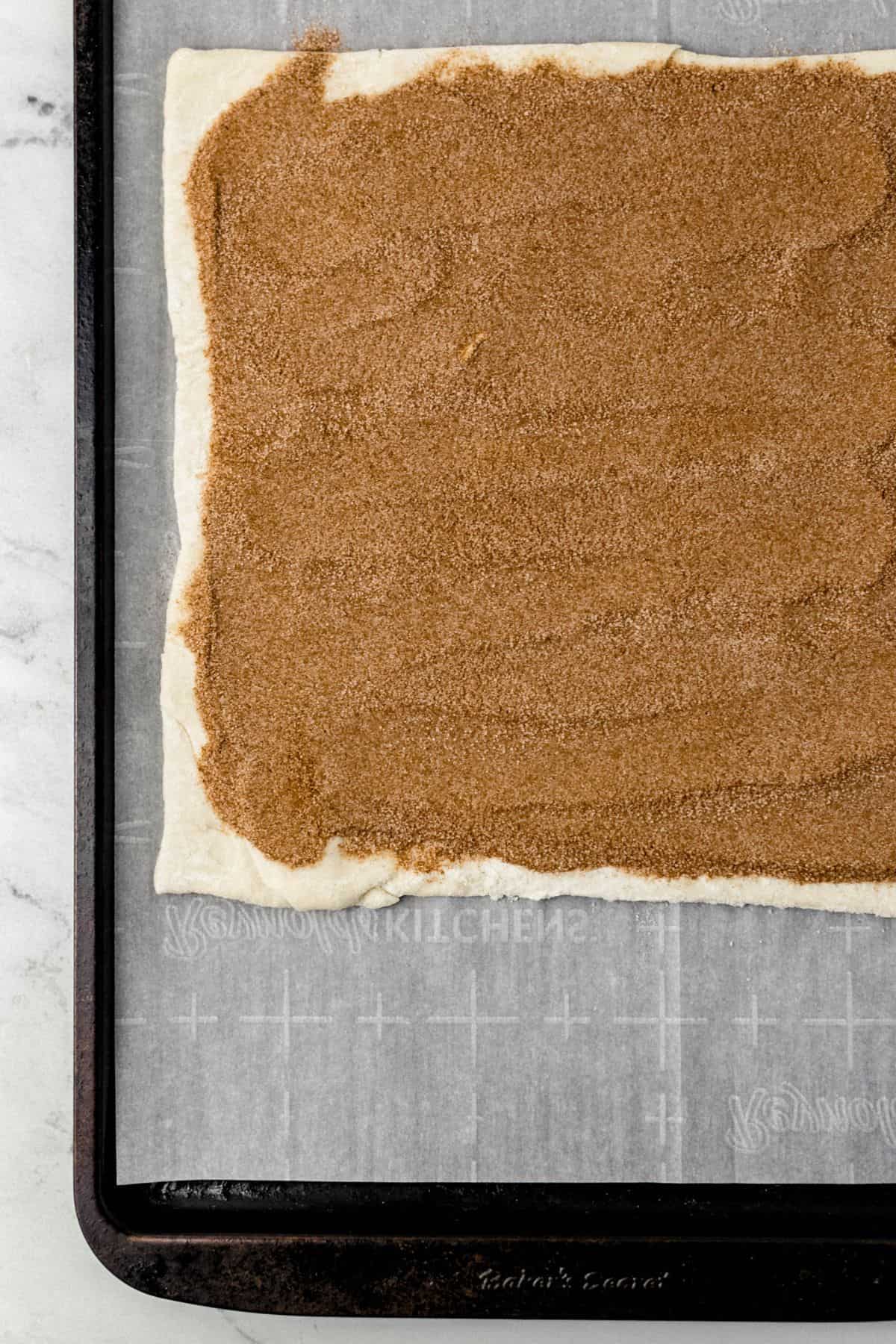 puff pastry dough topped with cinnamon sugar mixture on parchment lined baking sheet 