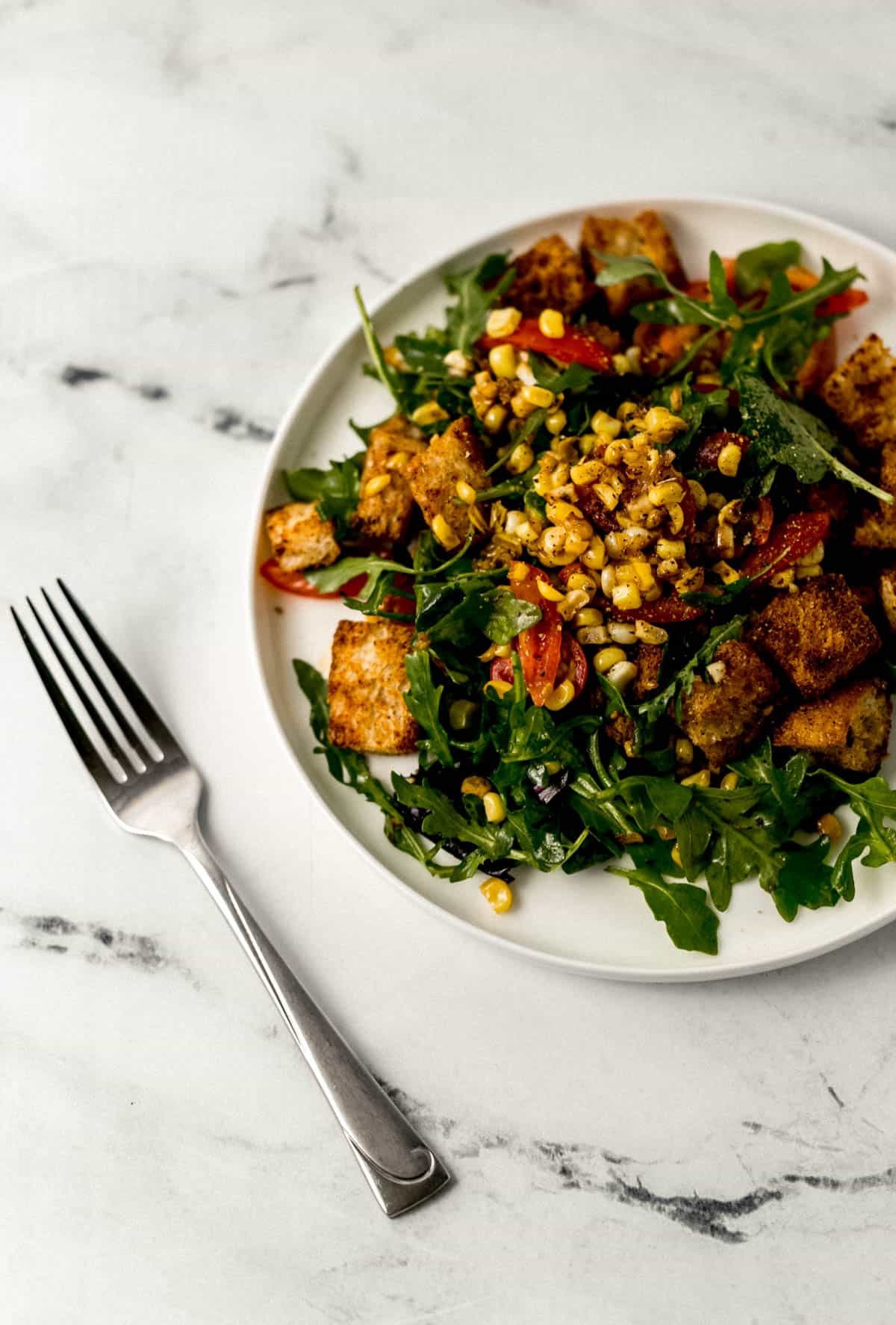 close up side view of salad on white plate beside a fork 