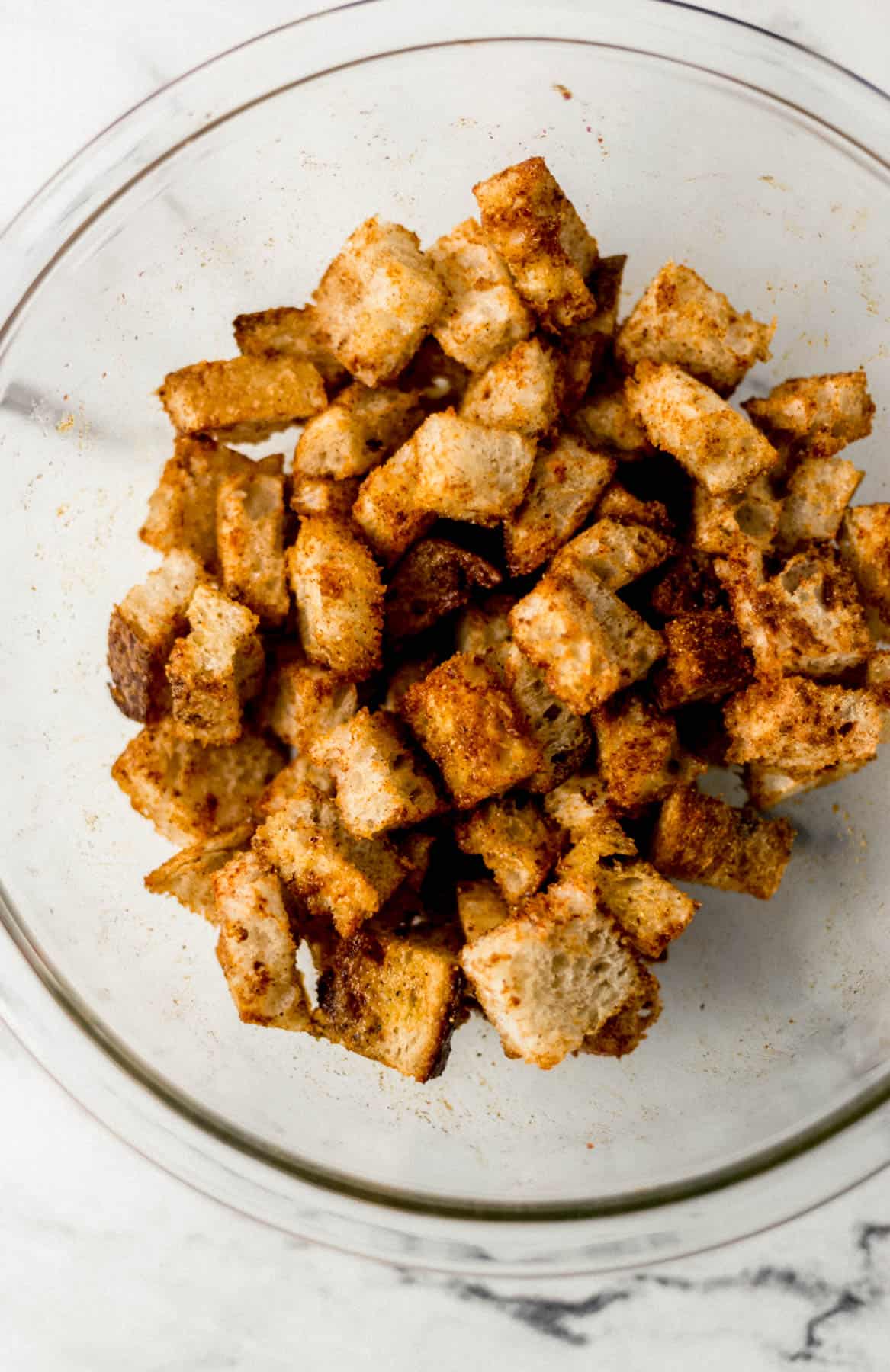 seasoned and buttered bread cubes in glass mixing bowl 