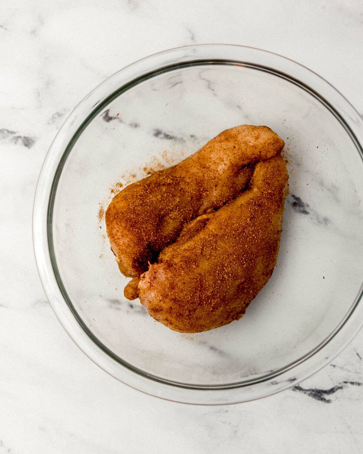 Seasoned chicken in a large glass mixing bowl.