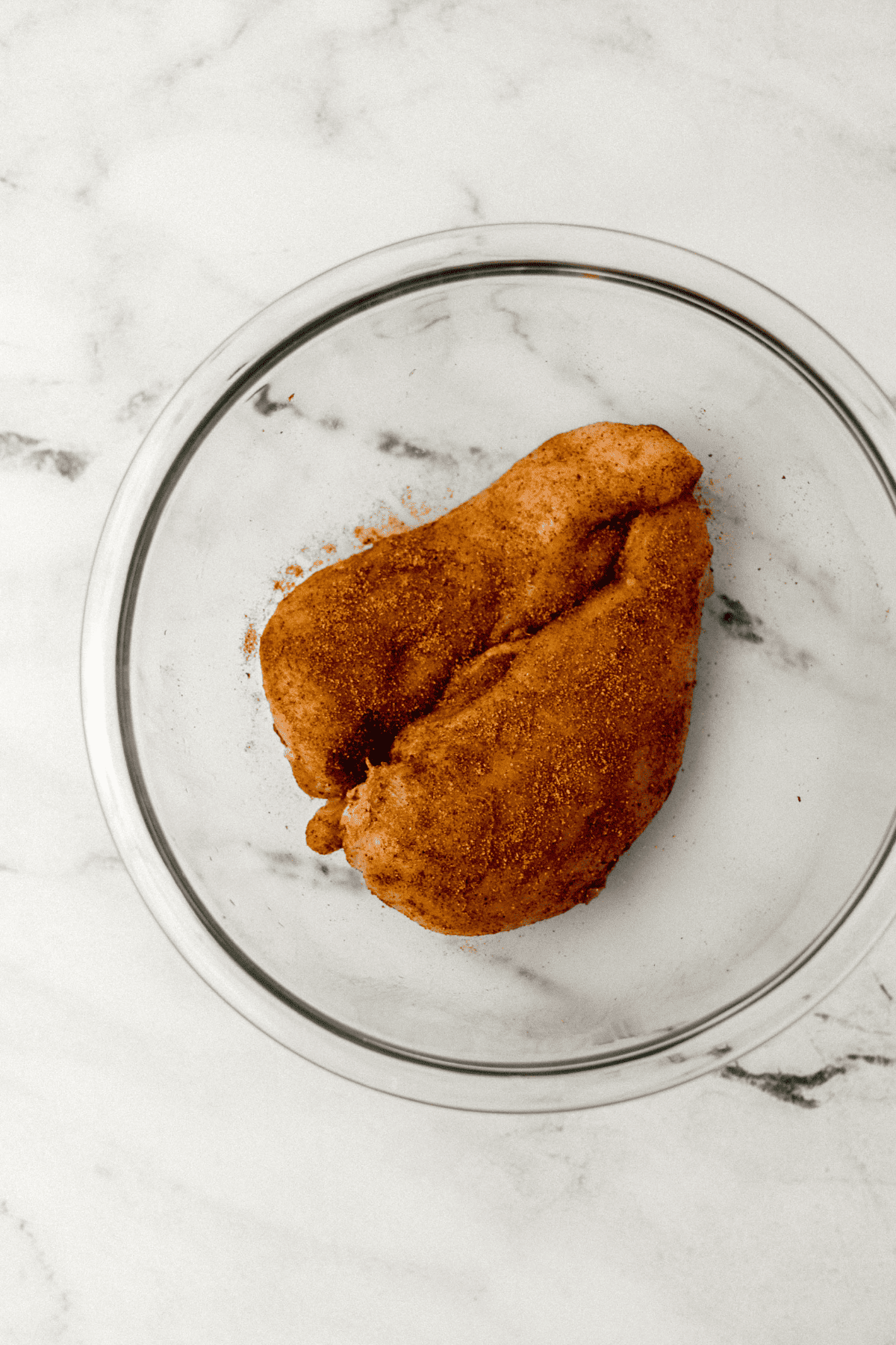 seasoned raw chicken in large glass mixing bowl