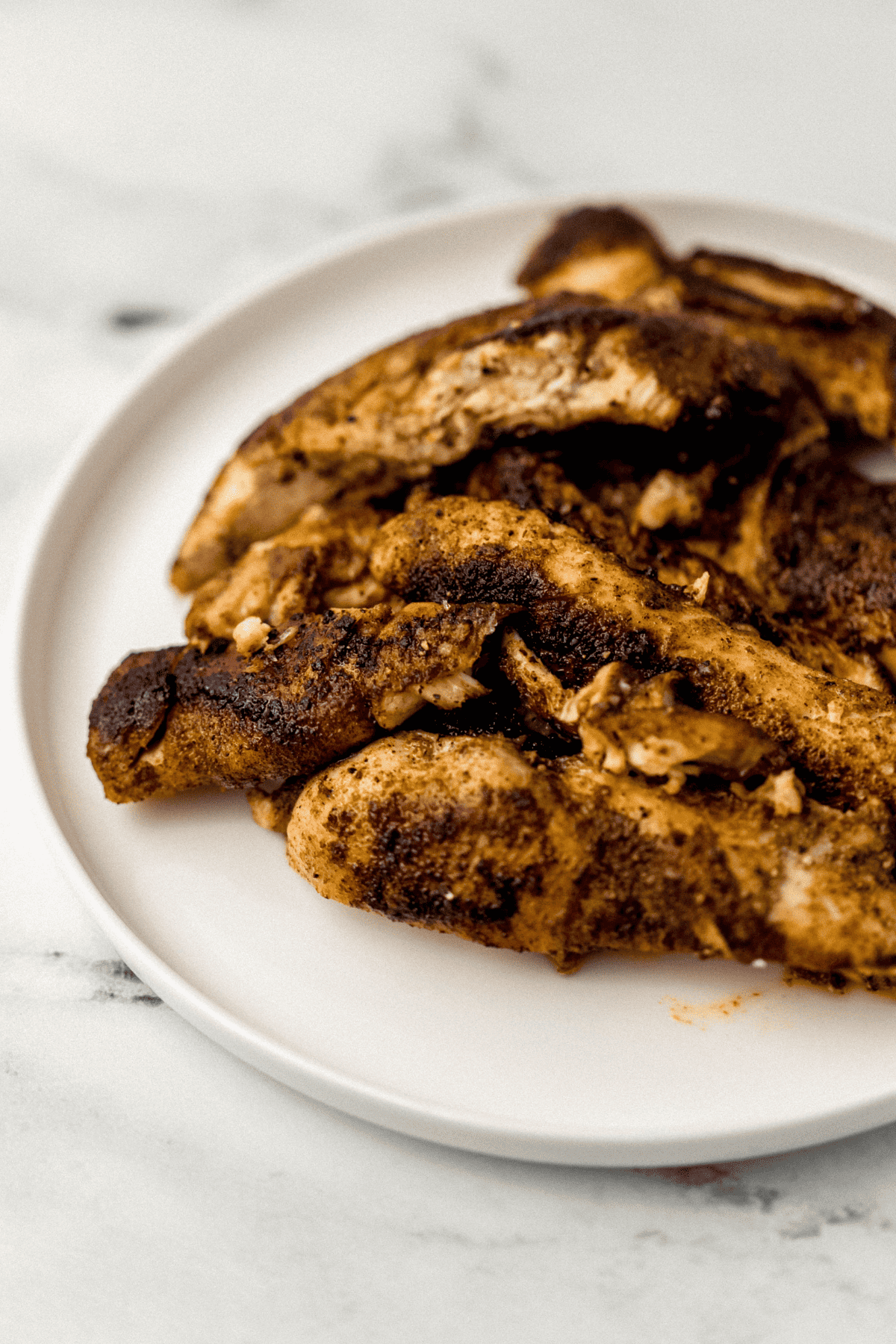 close up side view of cooked seasoned chicken on white plate