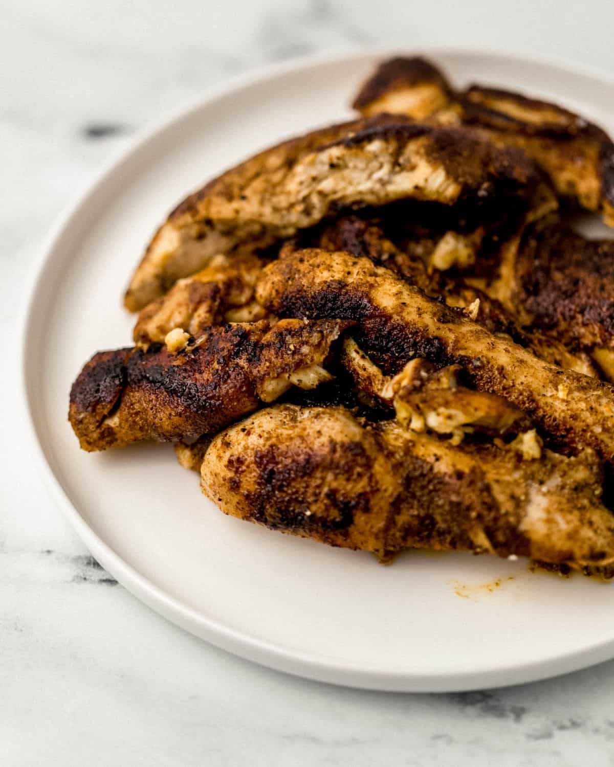 Close up front view of finished jerk chicken on white plate on marble surface.