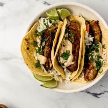 Overhead view of three finished tacos in a bowl by a small bowl of lime wedges.