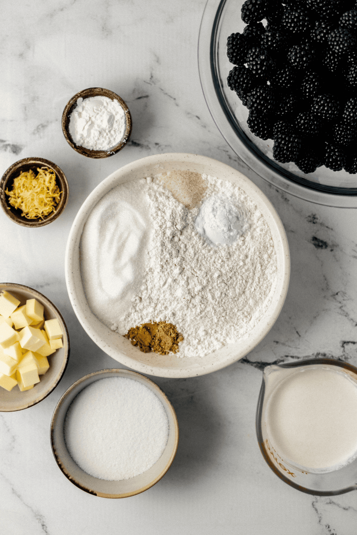ingredients needed to make blackberry cobbler in separate bowls on marble surface