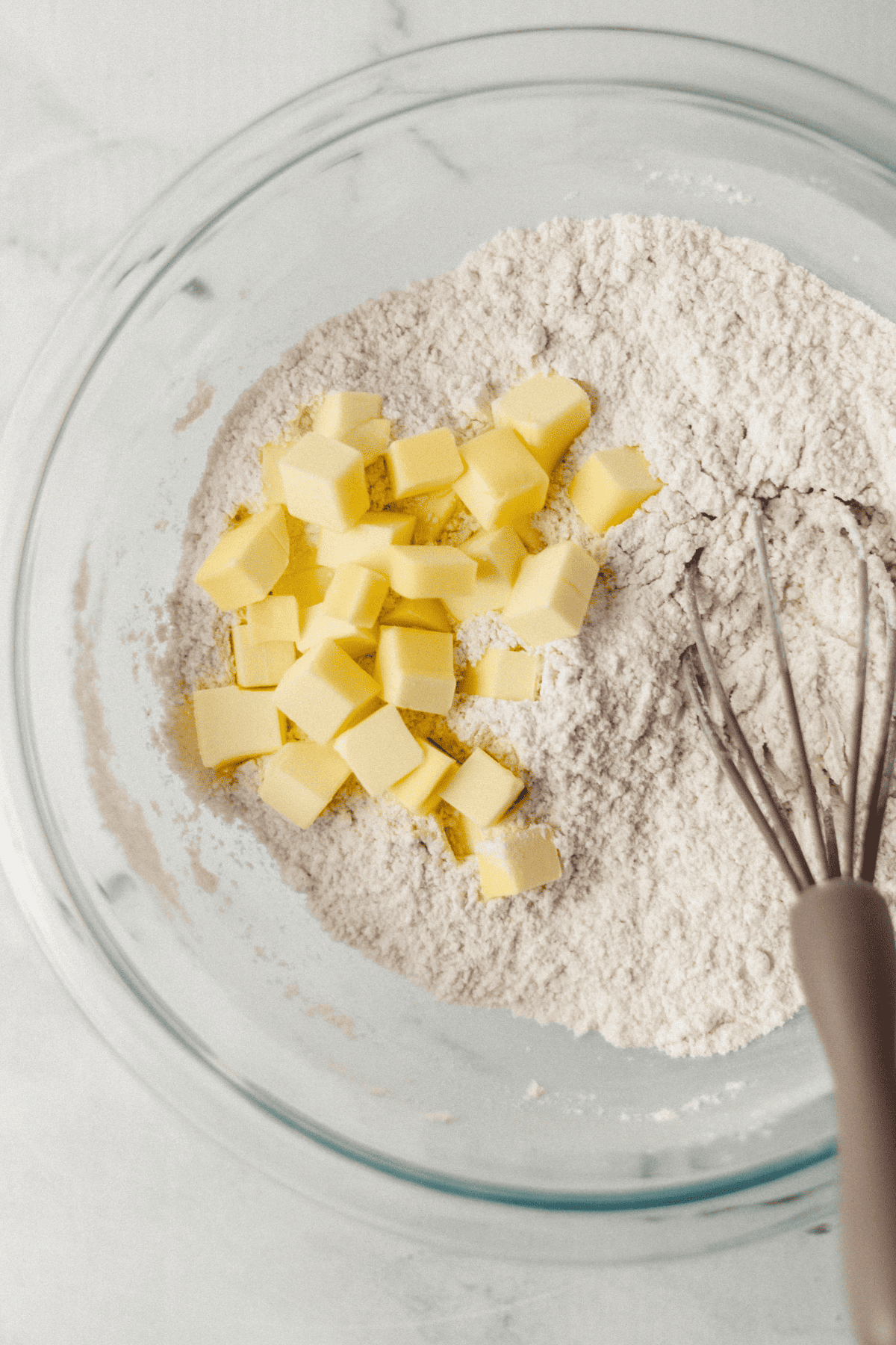 butter added to flour mixture in glass mixing bowl with whisk