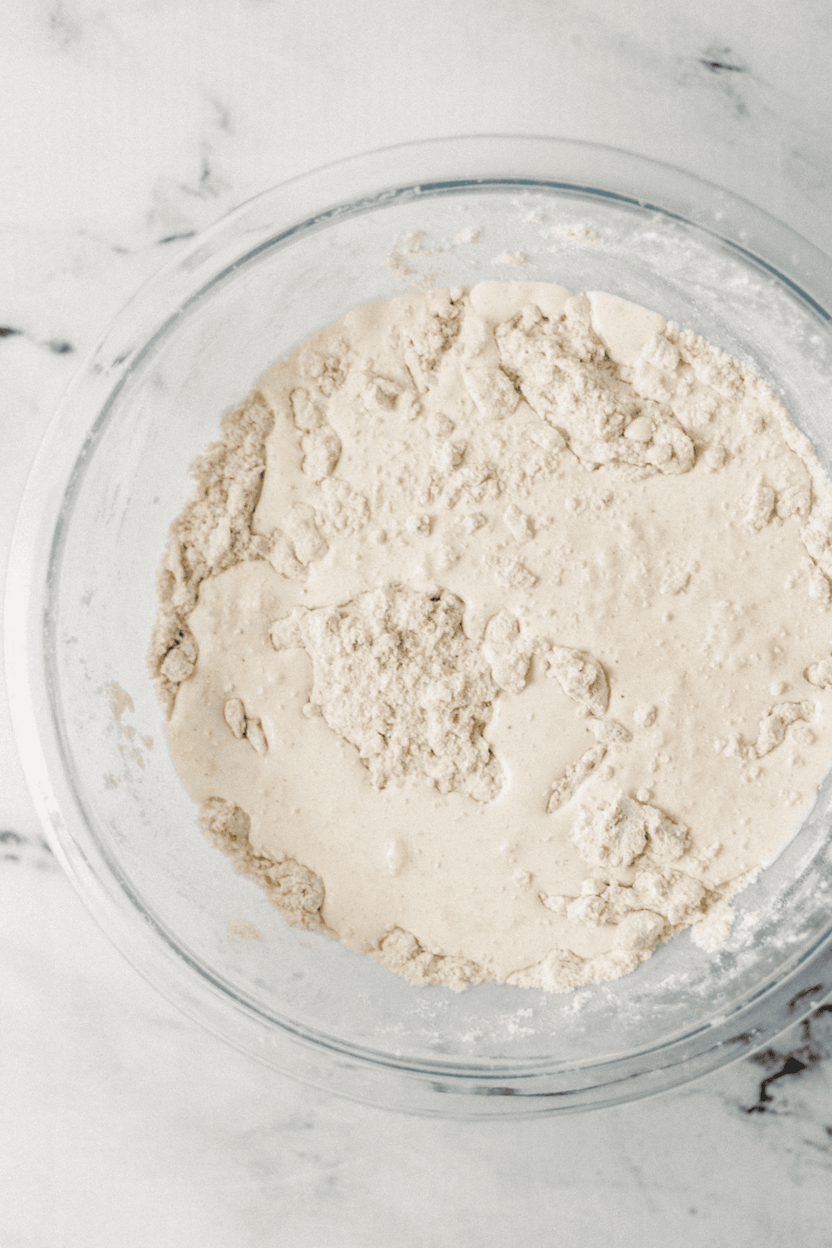 wet ingredients added to dry in glass mixing bowl on marble surface