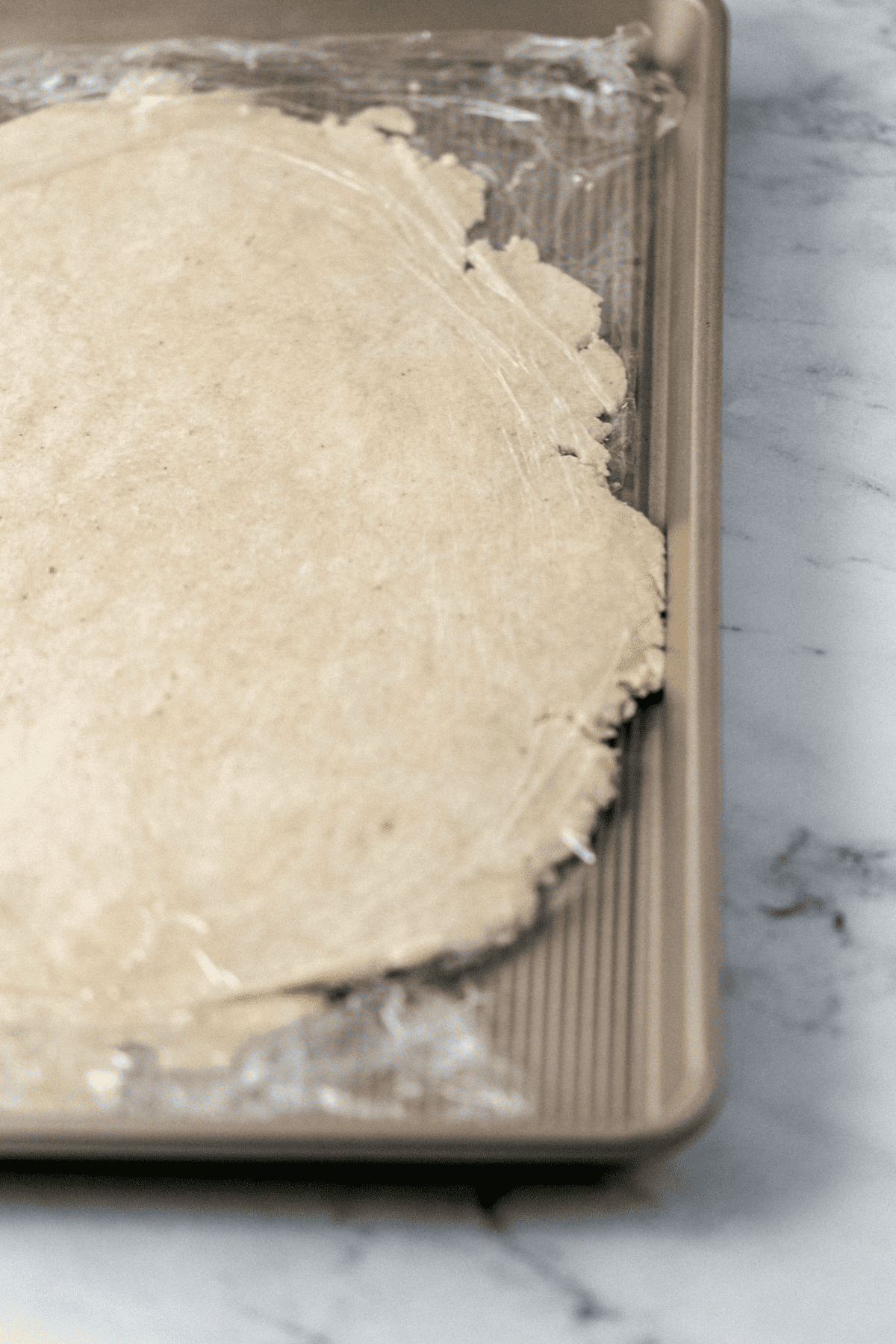 close up view of pie crust covered with plastic wrap on baking sheet