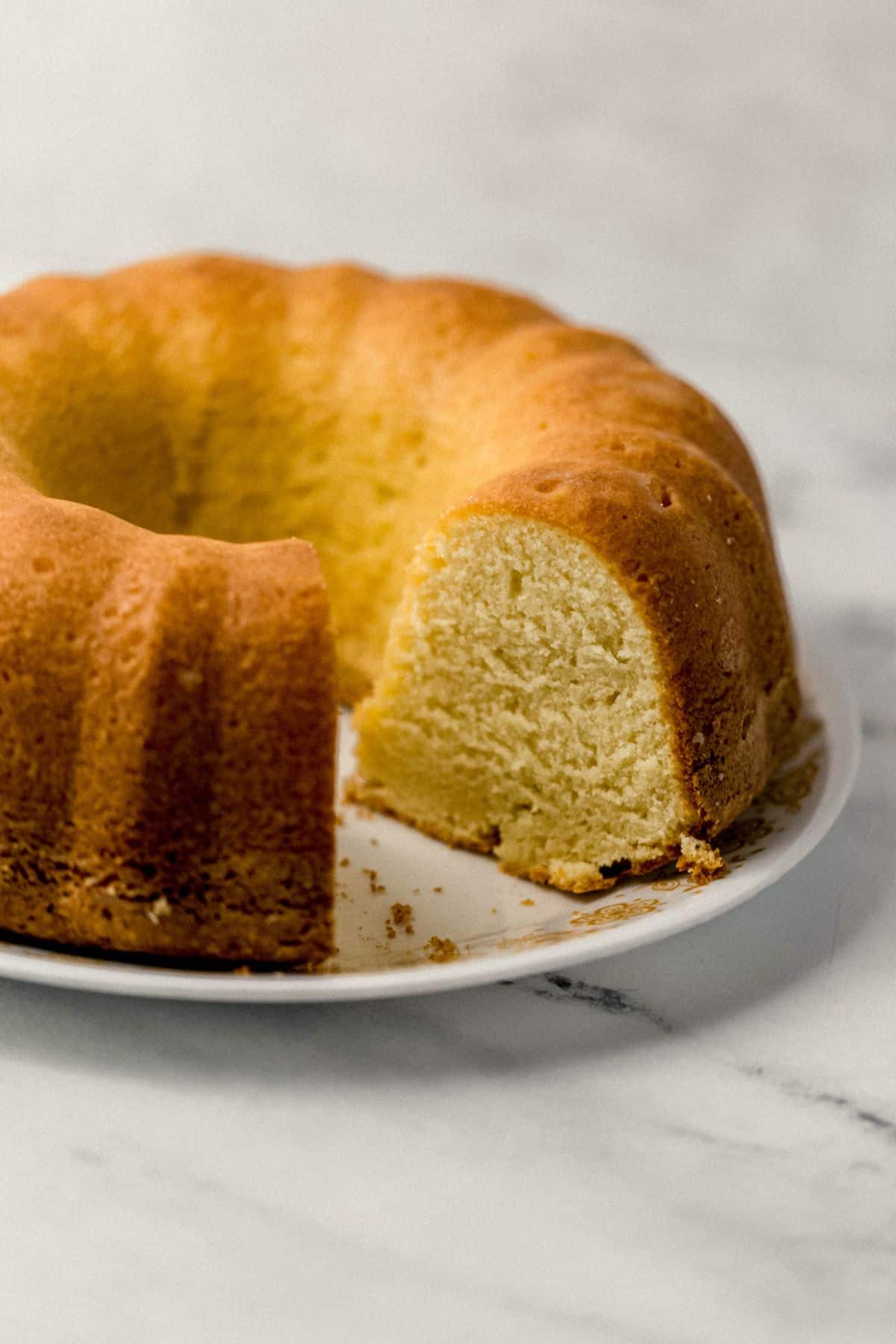 close up view of finished pound cake with a slice cut out of it on a white plate 
