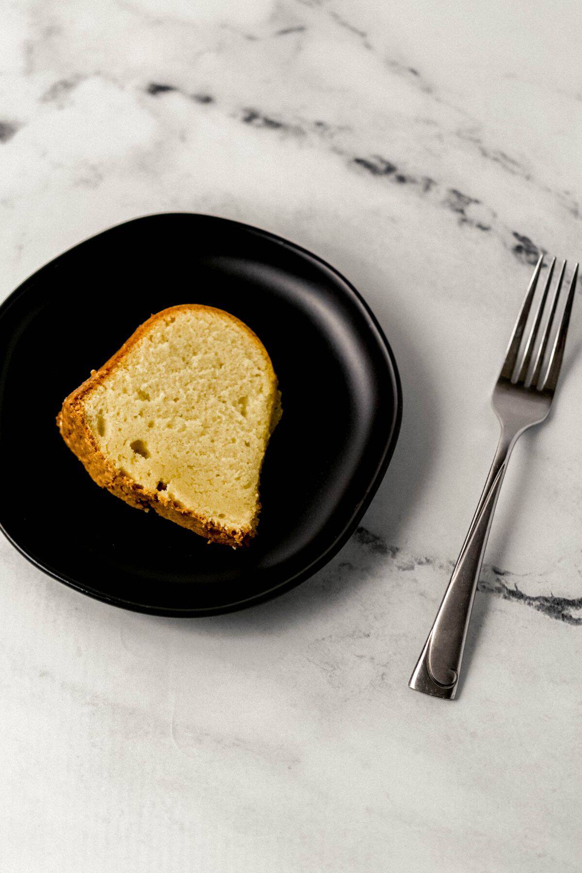 slice of cake on black plate beside a fork on marble surface 