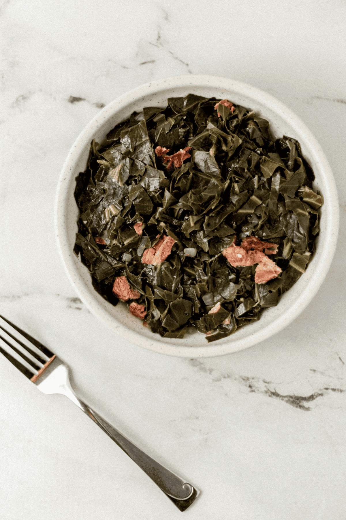 overhead view of greens in a bowl beside a fork on marble surface 