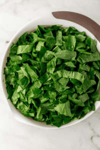 Overhead view of prepared fresh greens in large white bowl.