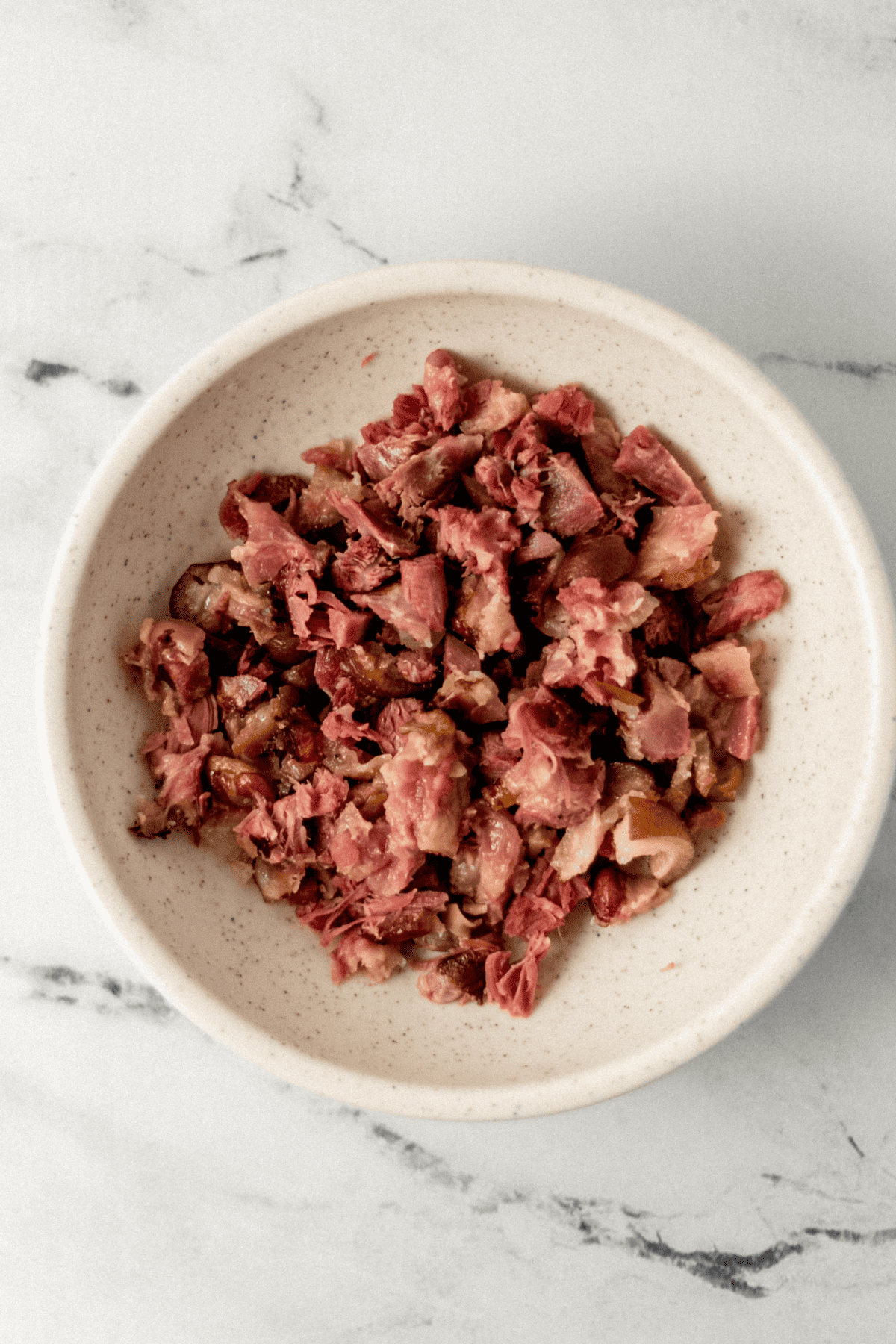 overhead view of chopped ham hocks in bowl on marble surface 