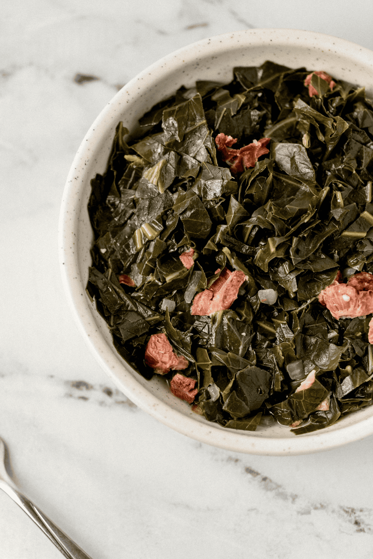 bowl of greens beside a fork on marble surface 