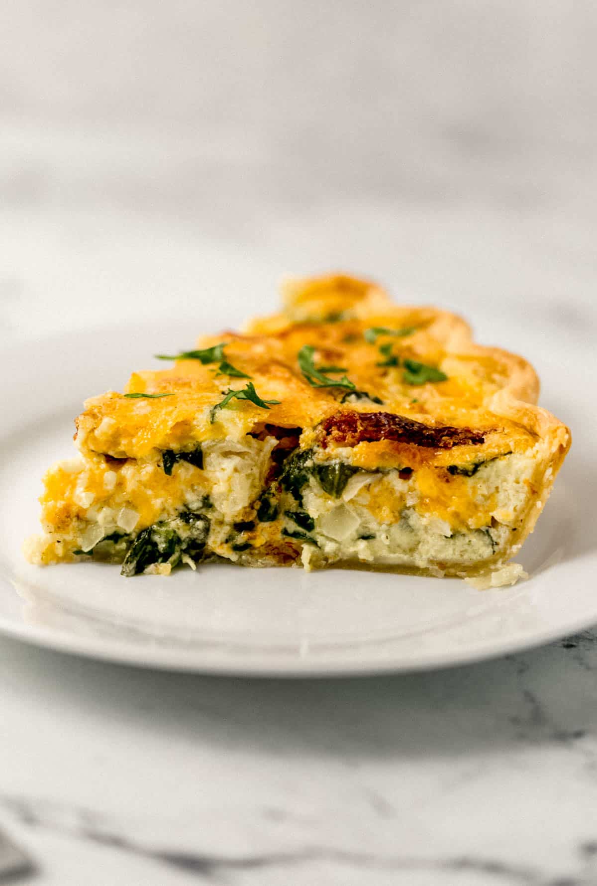 close up side view of single piece of quiche on a white plate 