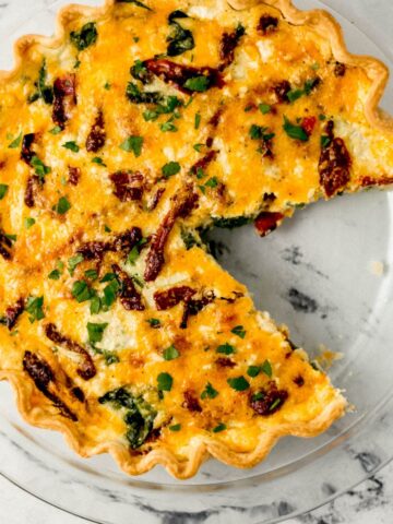 overhead view of baked quiche in a glass pie pan with a piece cut out of it