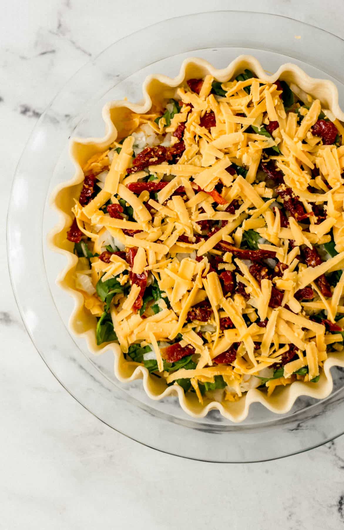 spinach, onion, tomatoes, and cheese added to pie crust in glass pie pan