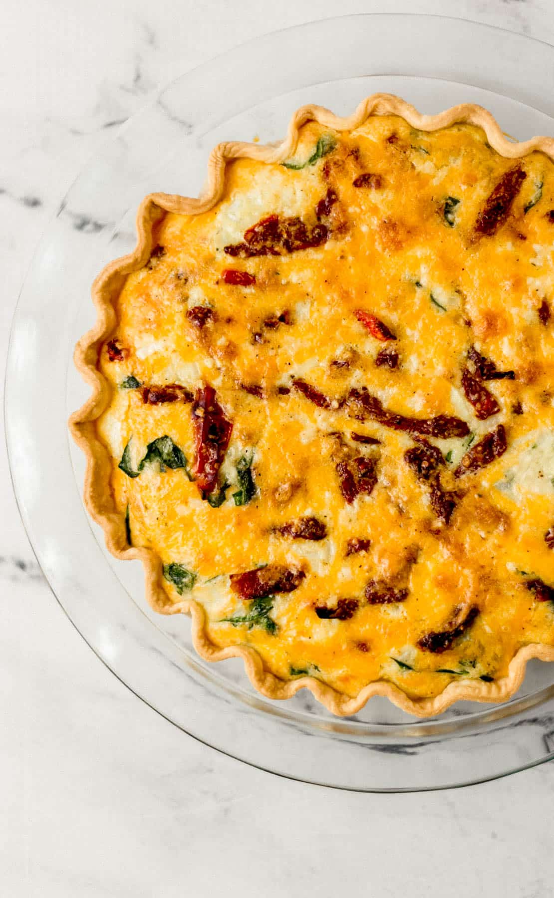overhead view of finished quiche in glass pie pan on marble surface
