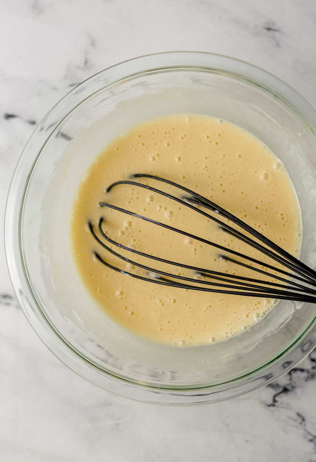 wet ingredients needed to make bread combined in glass mixing bowl with whisk