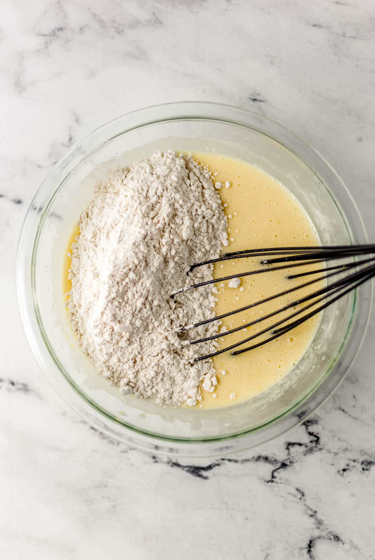 flour mixture added to glass mixing bowl with other ingredients and whisk