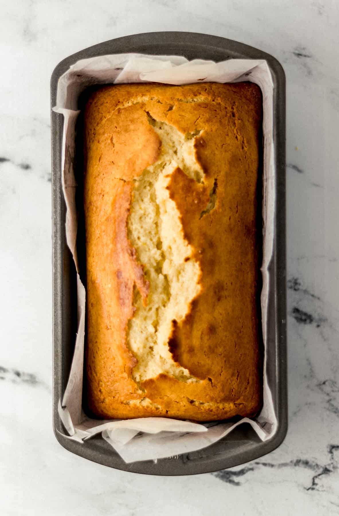 baked bread in parchment lined loaf pan on marble surface 