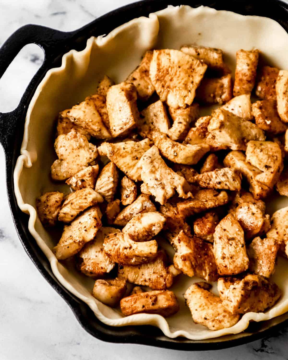 Pie dough topped with cooked chicken in cast iron skillet. 