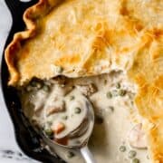 Overhead view of finished pot pie in cast iron skillet with serving spoon in it.